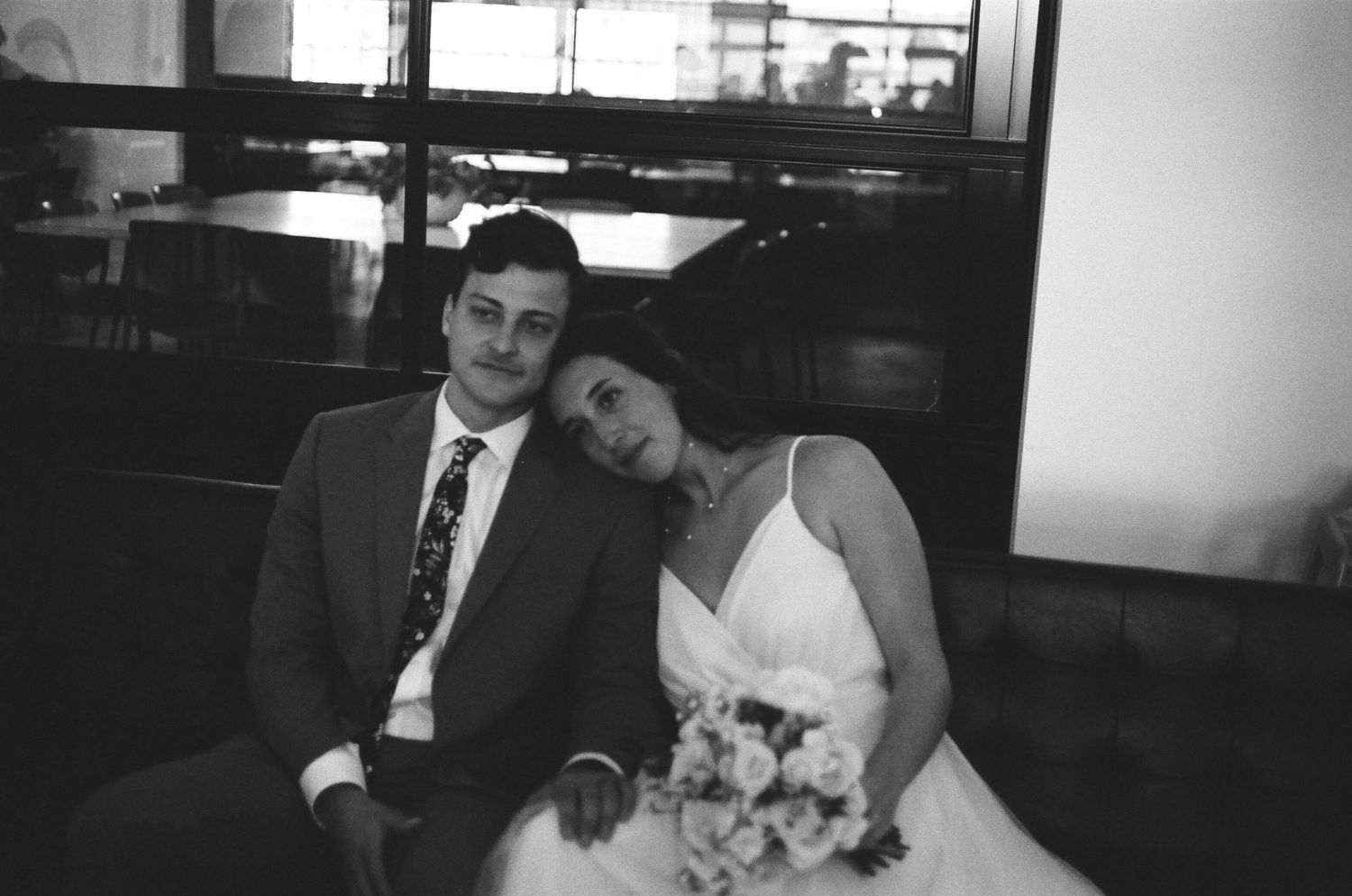 Wedding couple resting together in formal attire with bridal bouquet in black and white.