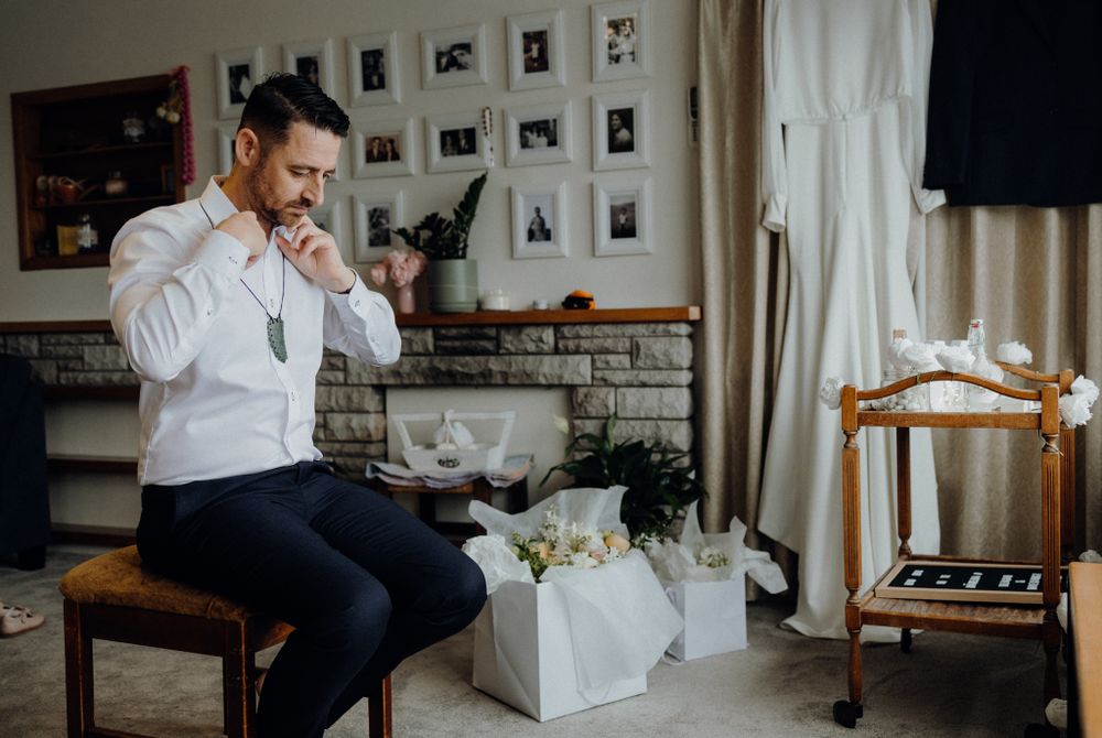 Wedding preparation moment showing formal attire adjustments in room with photo wall.