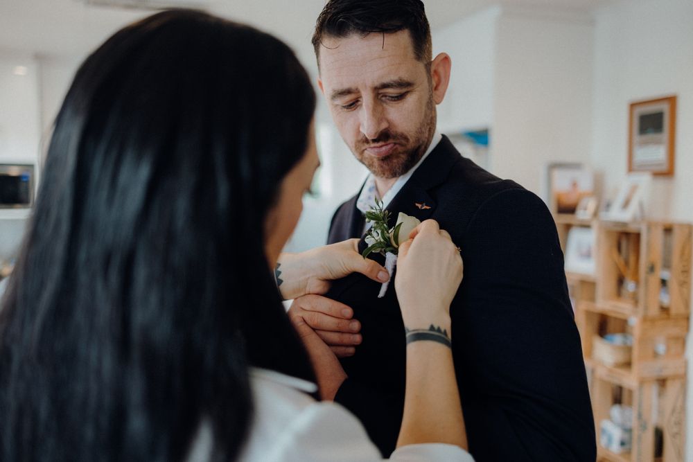 Intimate wedding preparation moment showing boutonniere being pinned on lapel.