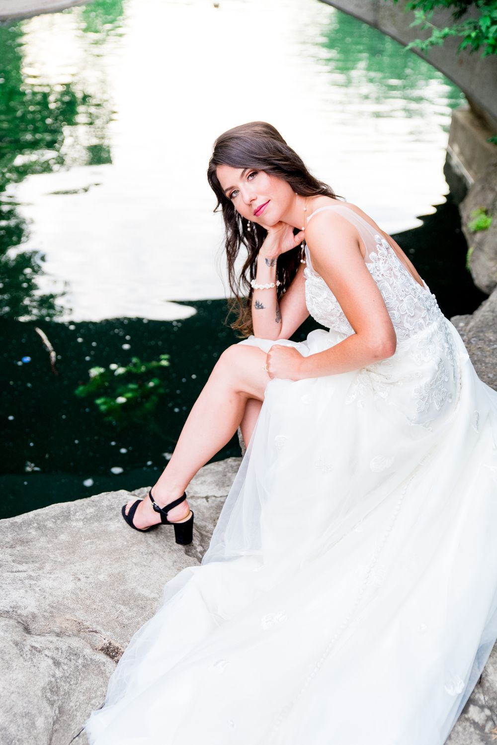 bride in black heels leans onto her knee, wedding dress fanned out showing off her leg