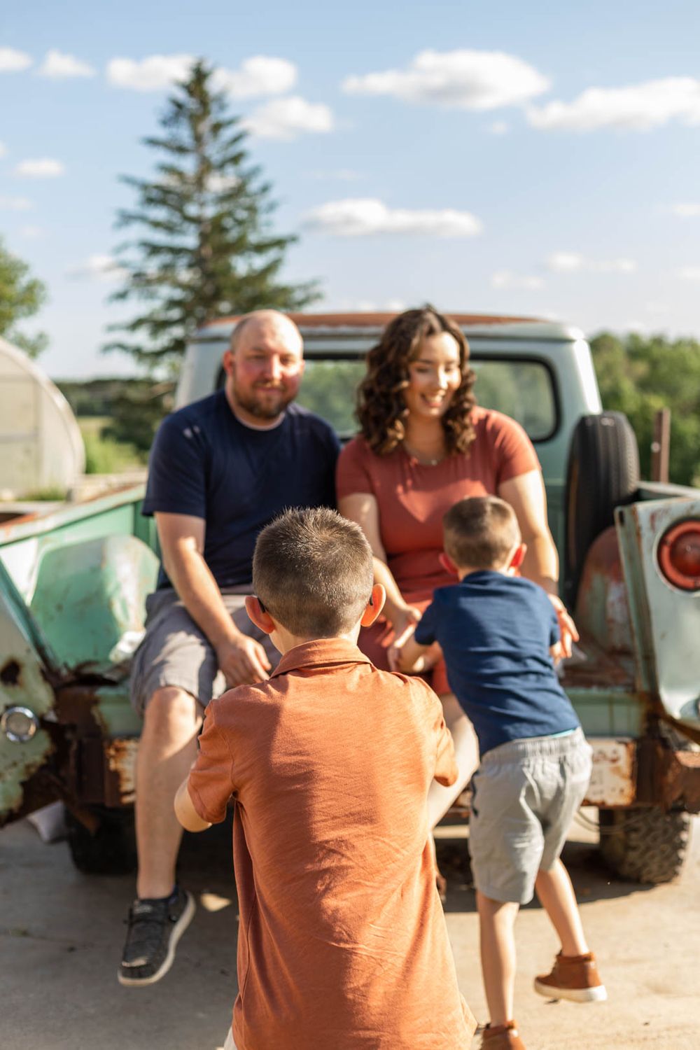 A casual family gathering around an old pickup truck on a sunny summer day.