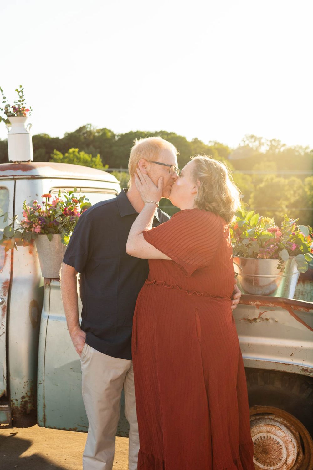 A loving moment shared beside a rustic truck decorated with flowers at sunset.