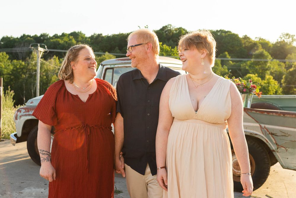 Three people sharing joyful laughter against a vintage truck backdrop at golden hour.