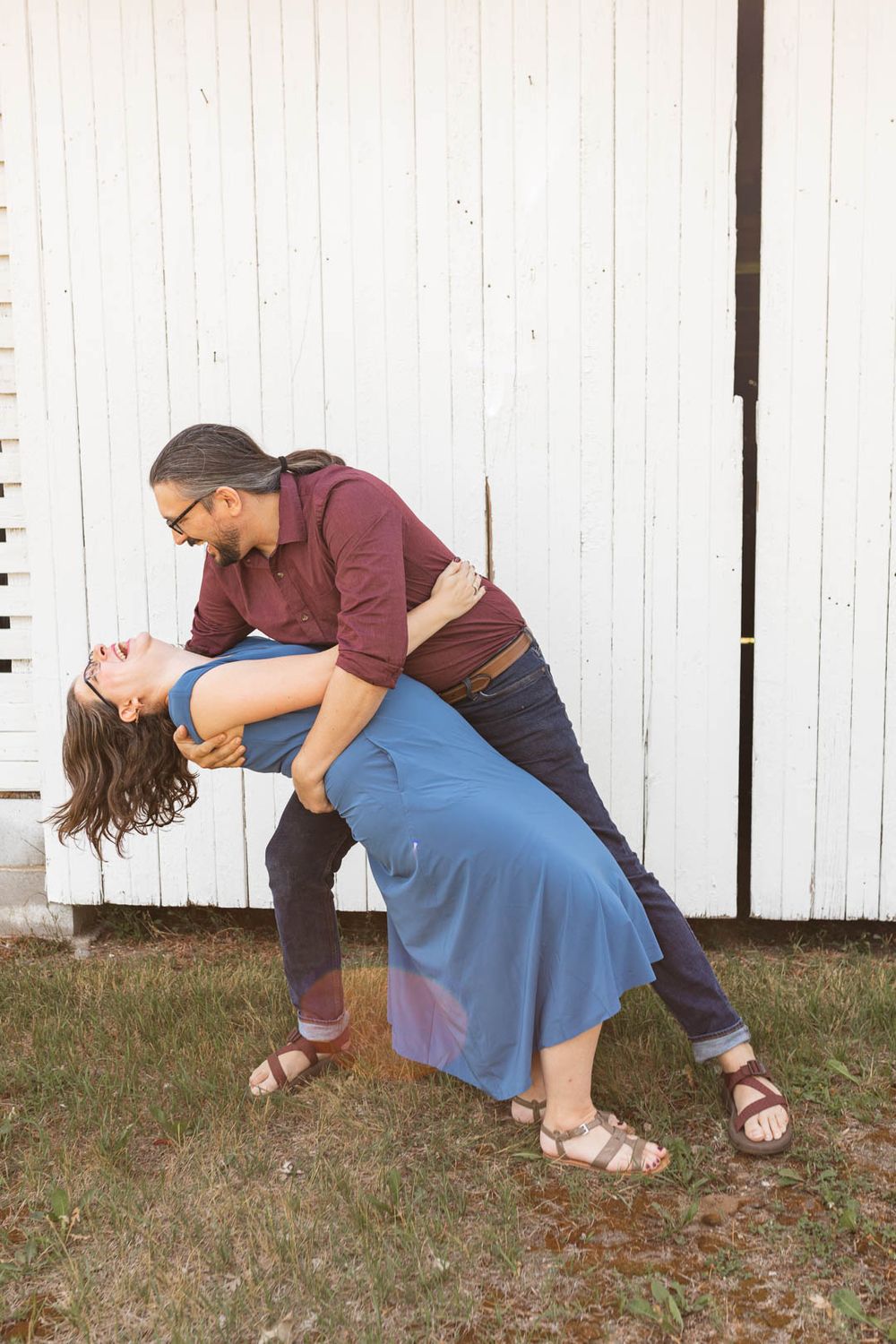 Playful dip pose against white barn wall during sunset photo session.