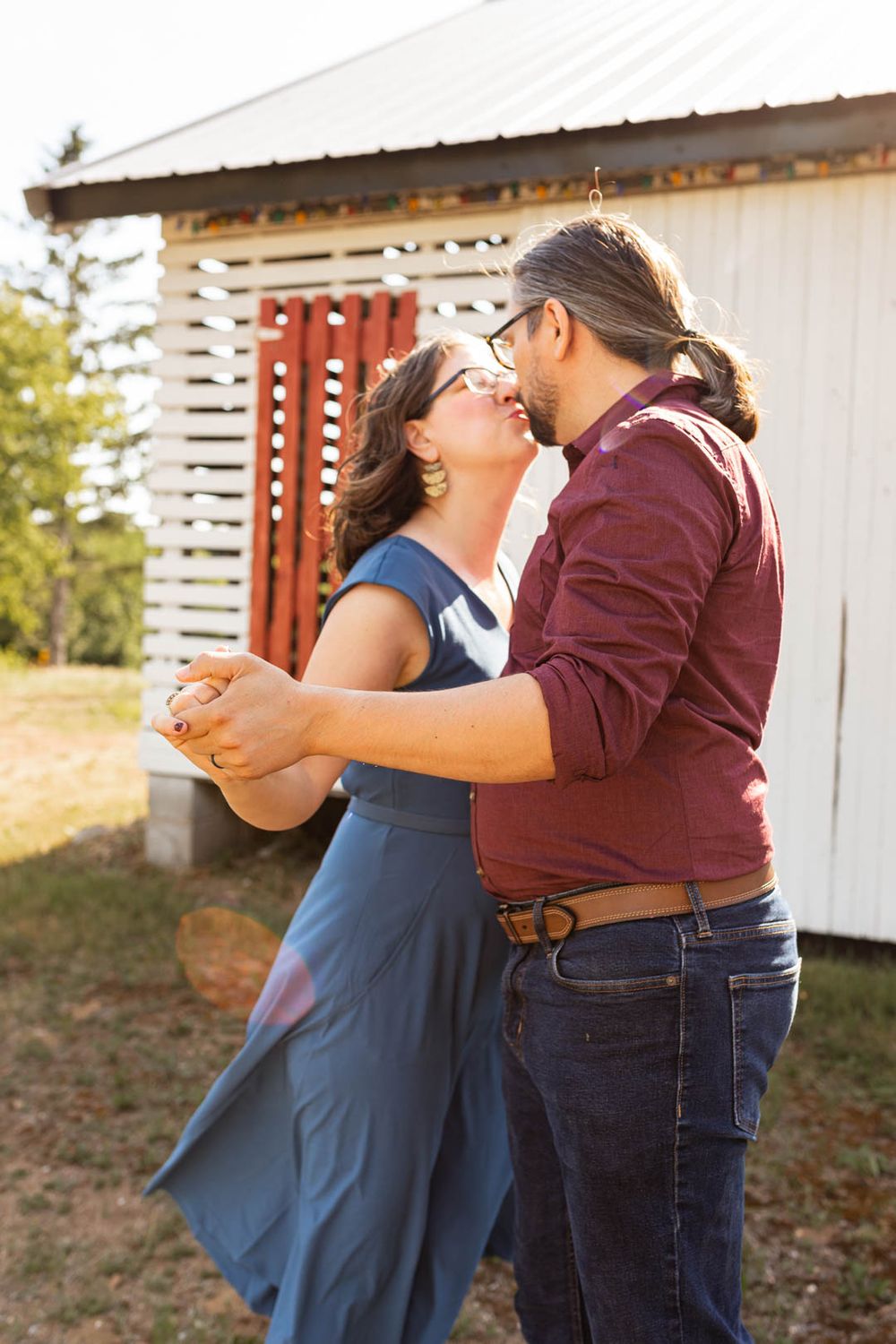 A romantic country dance scene with a couple in casual attire sharing a tender moment outside a rustic barn.