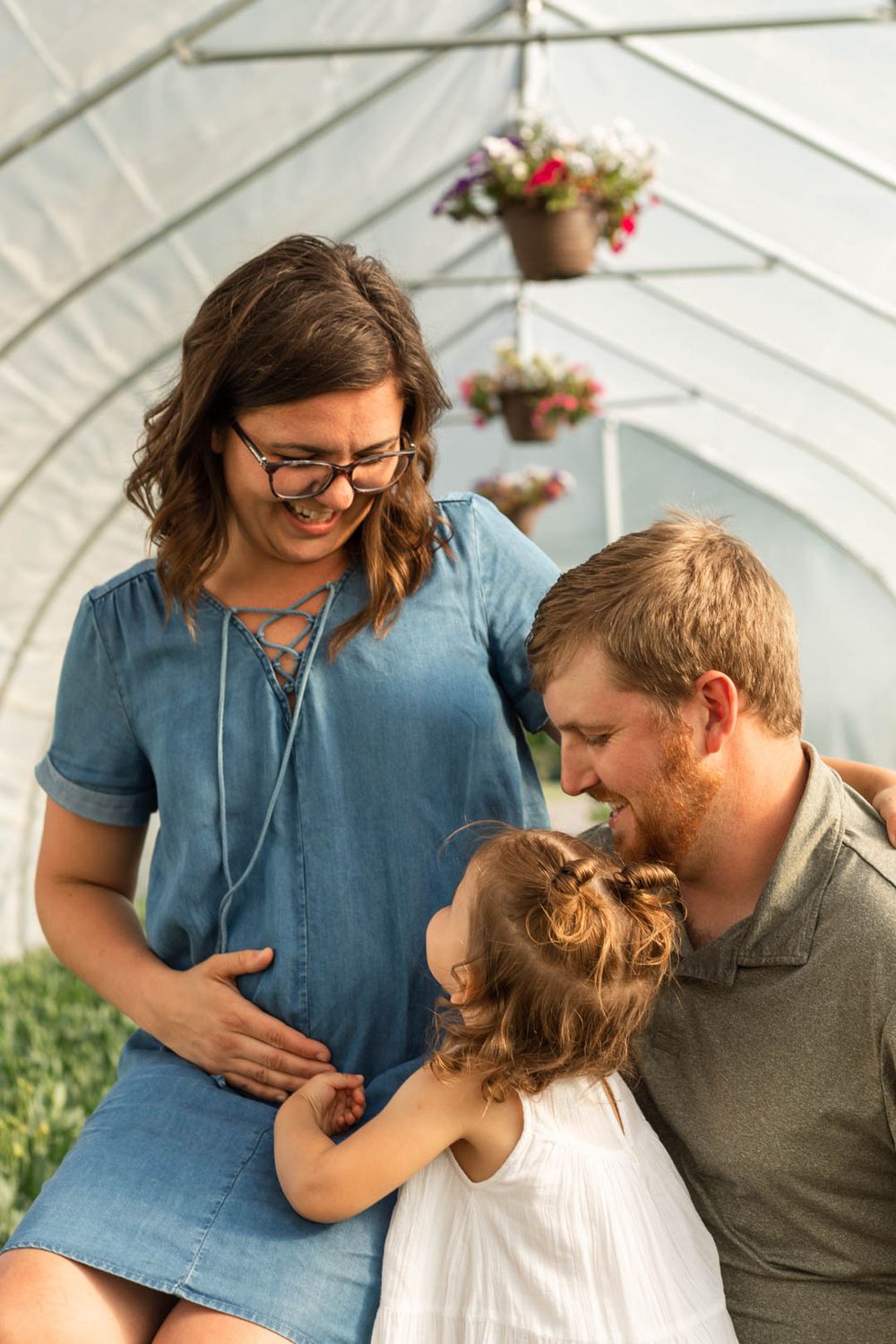 Family shares tender moment together in greenhouse with hanging flower baskets.