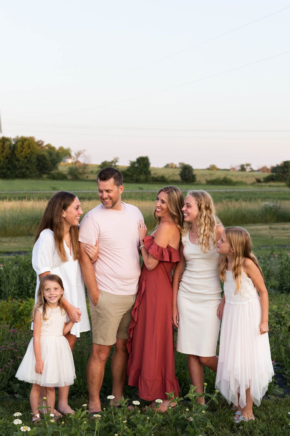 Family poses together in field at sunset wearing coordinated white and red outfits.
