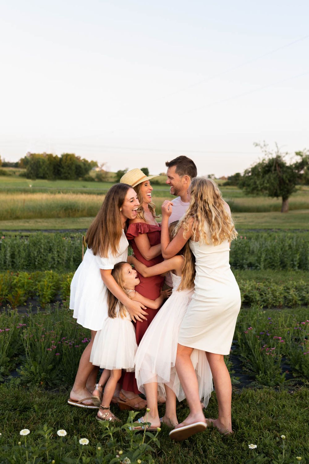 Family shares joyful group hug in blooming field at sunset.