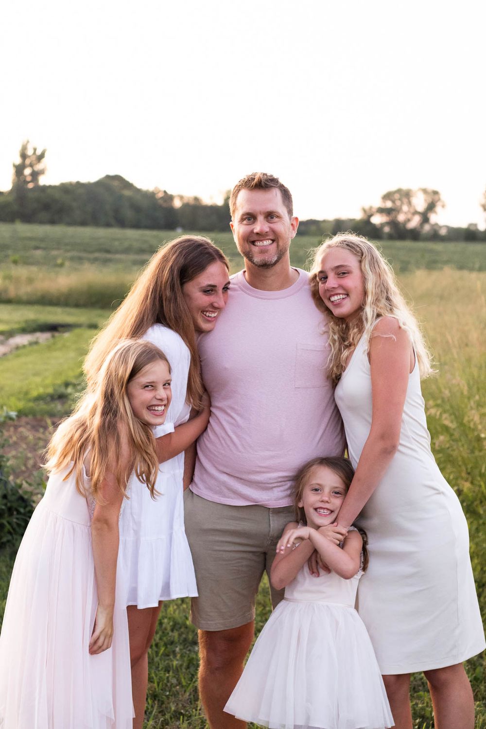 A happy family embraces while posing together in a sunset field.
