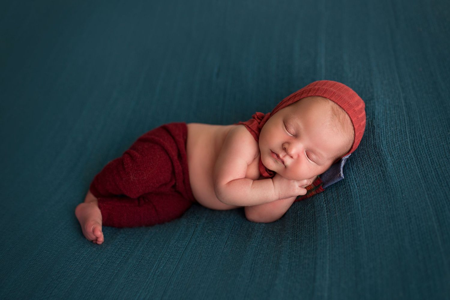newborn posed on side lay dressed in red clothing detres photography