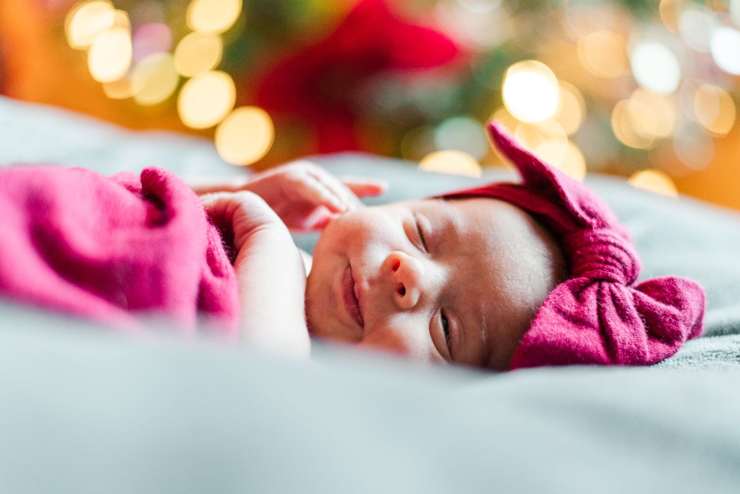 Lifestyle newborn baby in pink wrap in front of Christmas tree in Pittsburgh, Pennsylvania