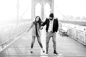 black and white photo of an engaged couple walking and laughing along Brooklyn Bridge in NYC at sunrise