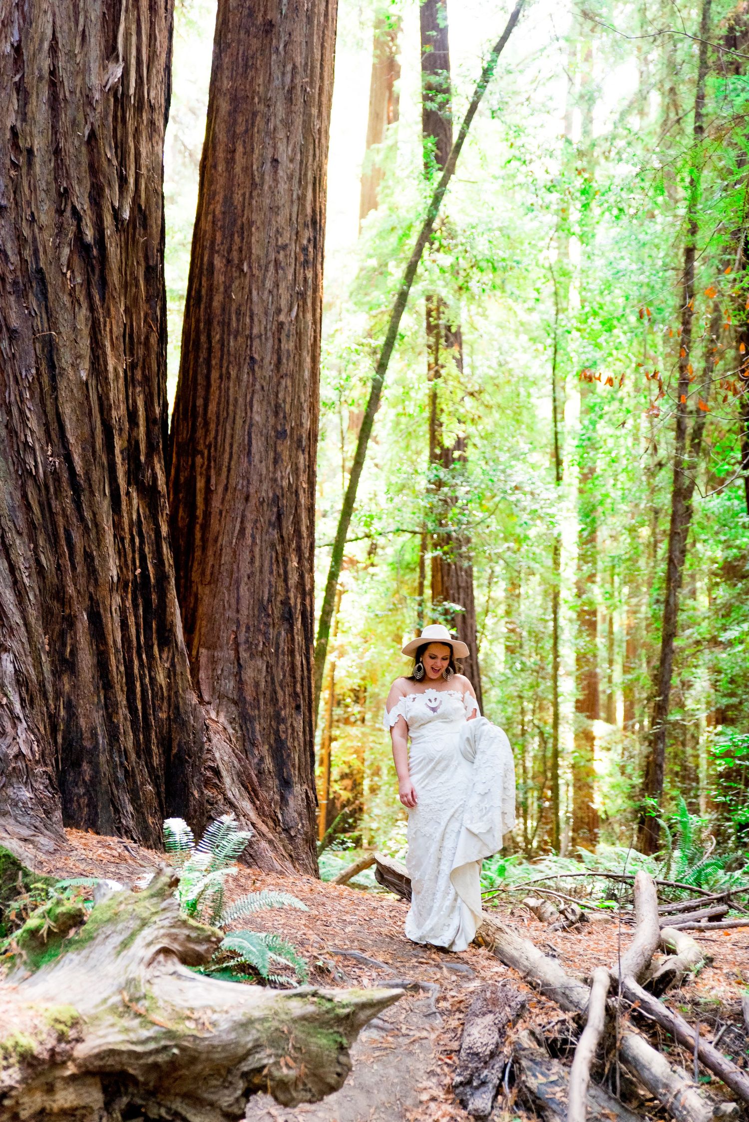 bride walks through Redwoods carrying her wedding dress in Northern California Wedding