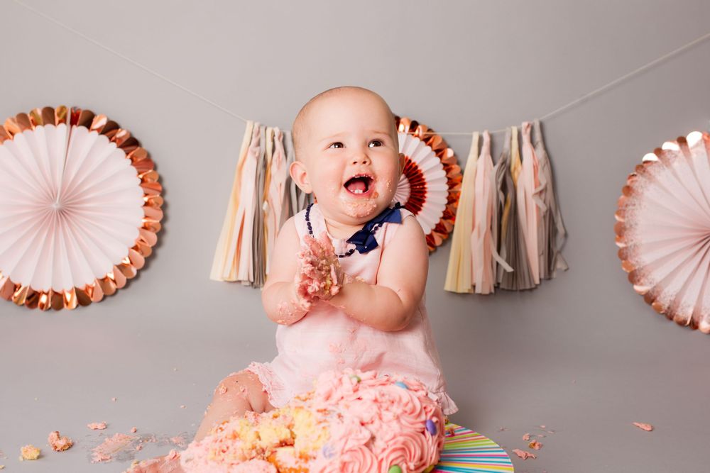 A baby girl claps her hands together during her cake smash photo shoot - Family Photography