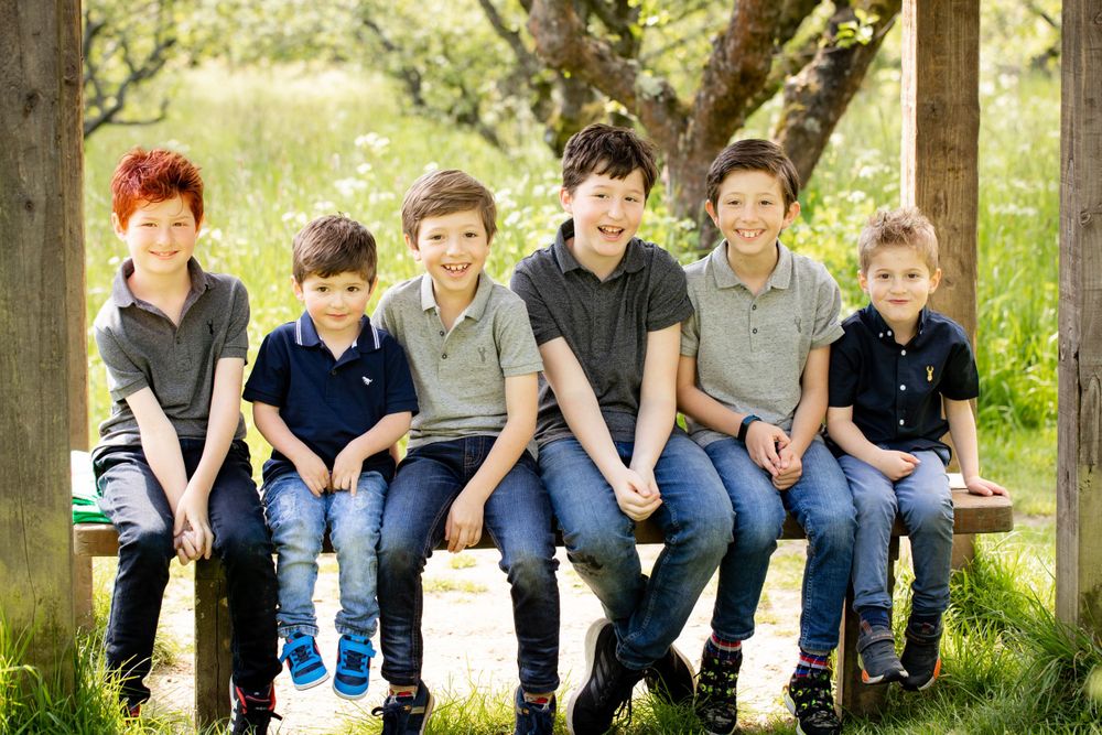 Six young boys smile as they pose together on a bench n the park - Family Photography