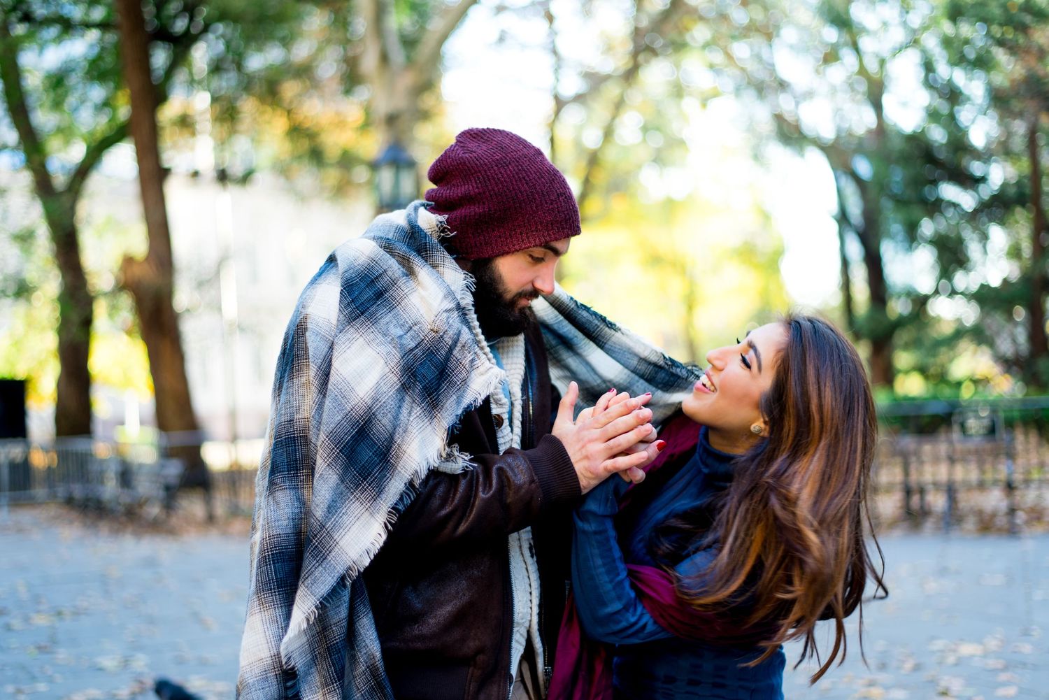 young engaged couple wrapped in navy plaid blanket holding hands and smiling for engagement pictures in NYC