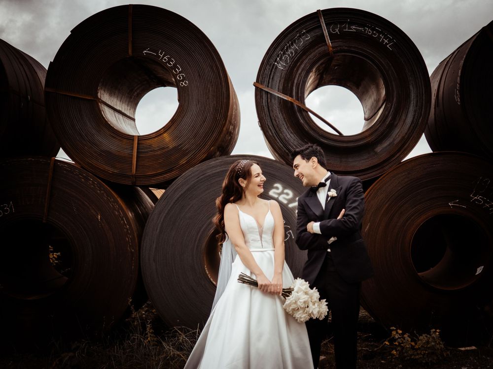 A romantic wedding couple poses together in front of large wooden wine barrels at a rustic winery.