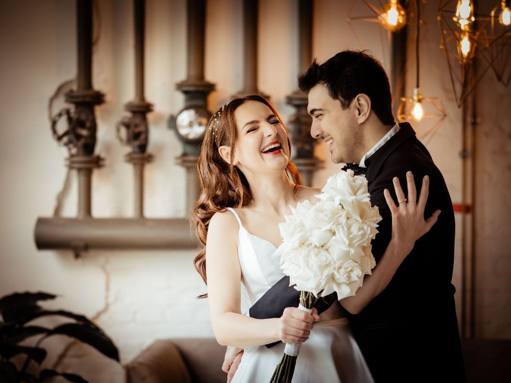 A joyful couple shares an intimate moment with white flowers while celebrating their wedding day in an industrial-style setting.
