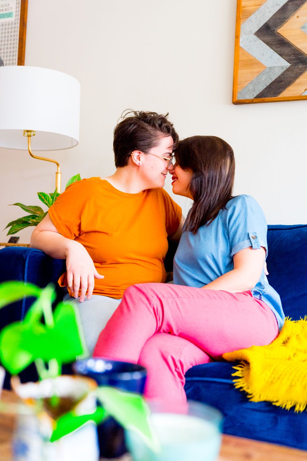 two women with foreheads together smiling on a blue couch with yellow blanket next to them
