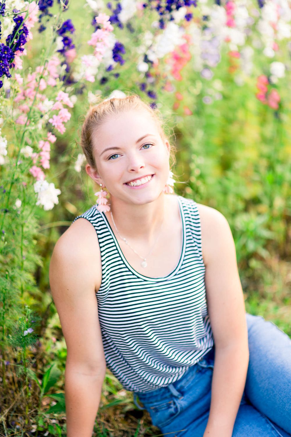 young woman with pink tassel earrings and striped tank top sitting in front of pink and purple flowers