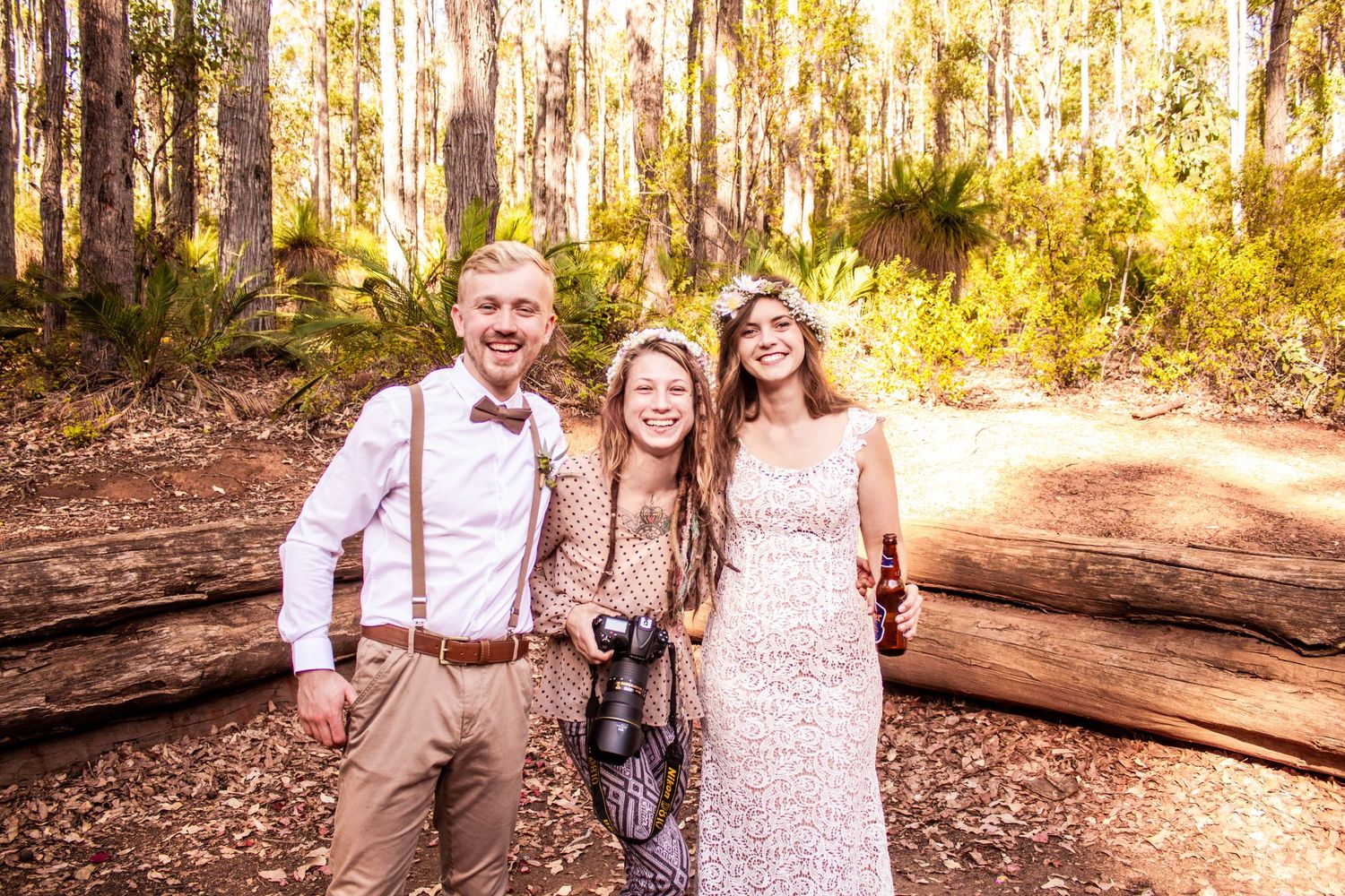 Three people pose together on forest trail with sun filtering through eucalyptus trees.
