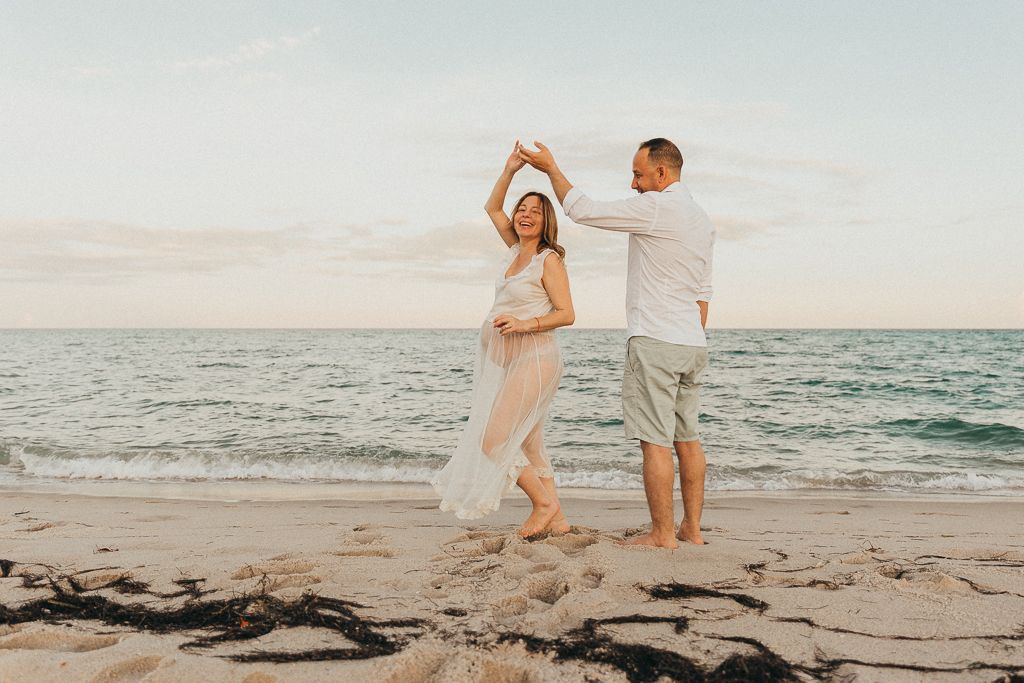 pregnant woman dancing with her husband on the beach