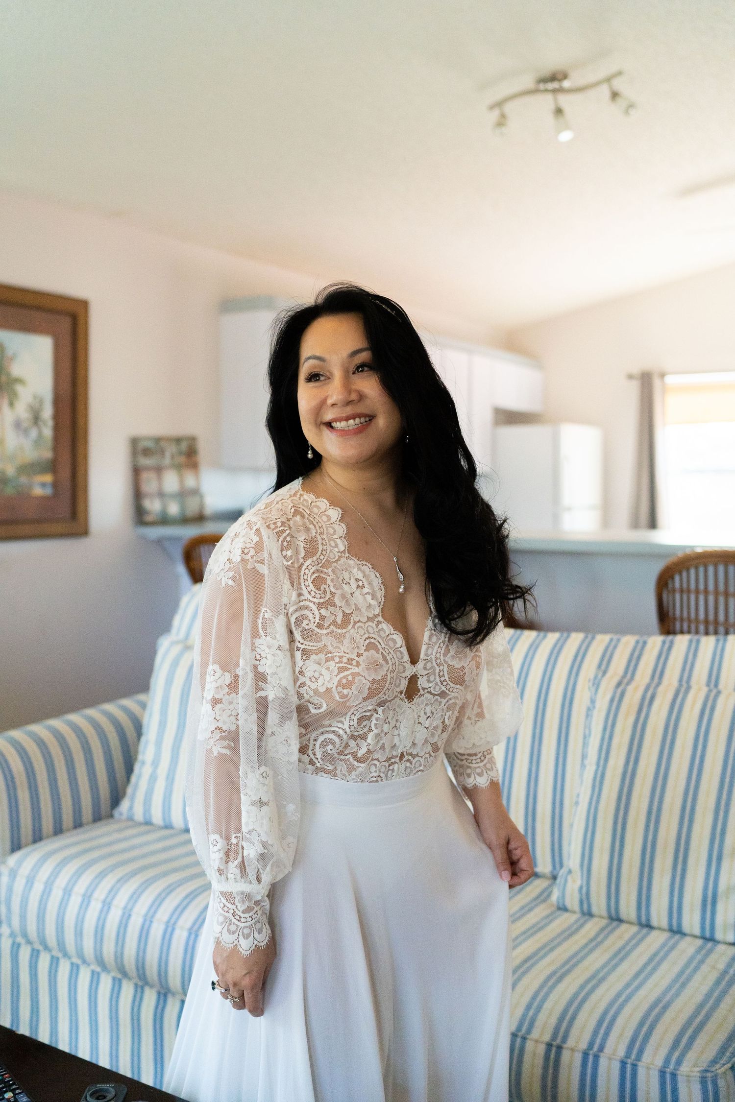 A lace-detailed white wedding dress displayed on a blue and white striped couch.