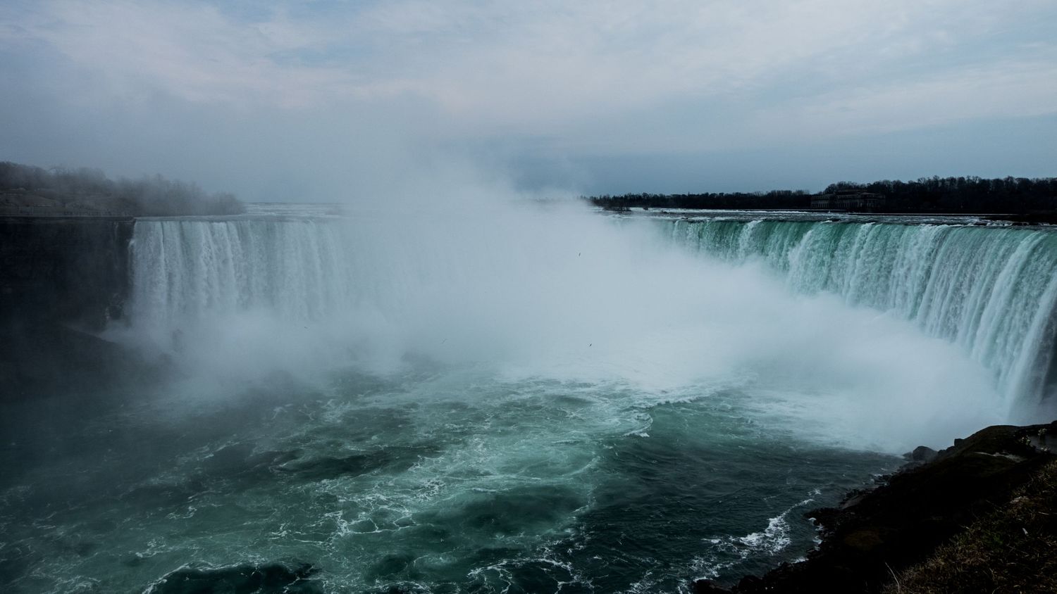 A massive horseshoe shaped water fall on an overcast day, full of mist