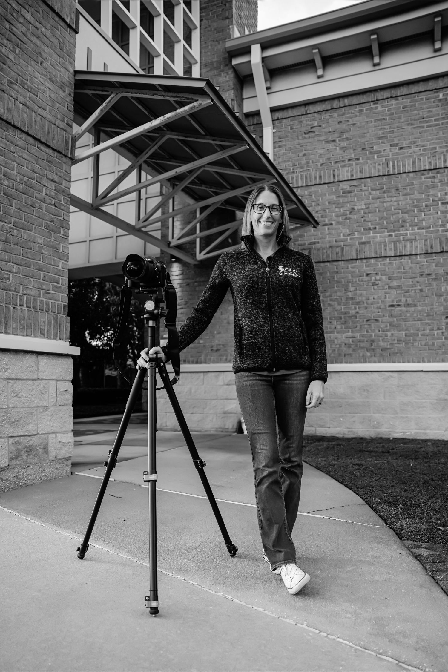 Camera equipment on tripod set up outside brick building in black and white photography.