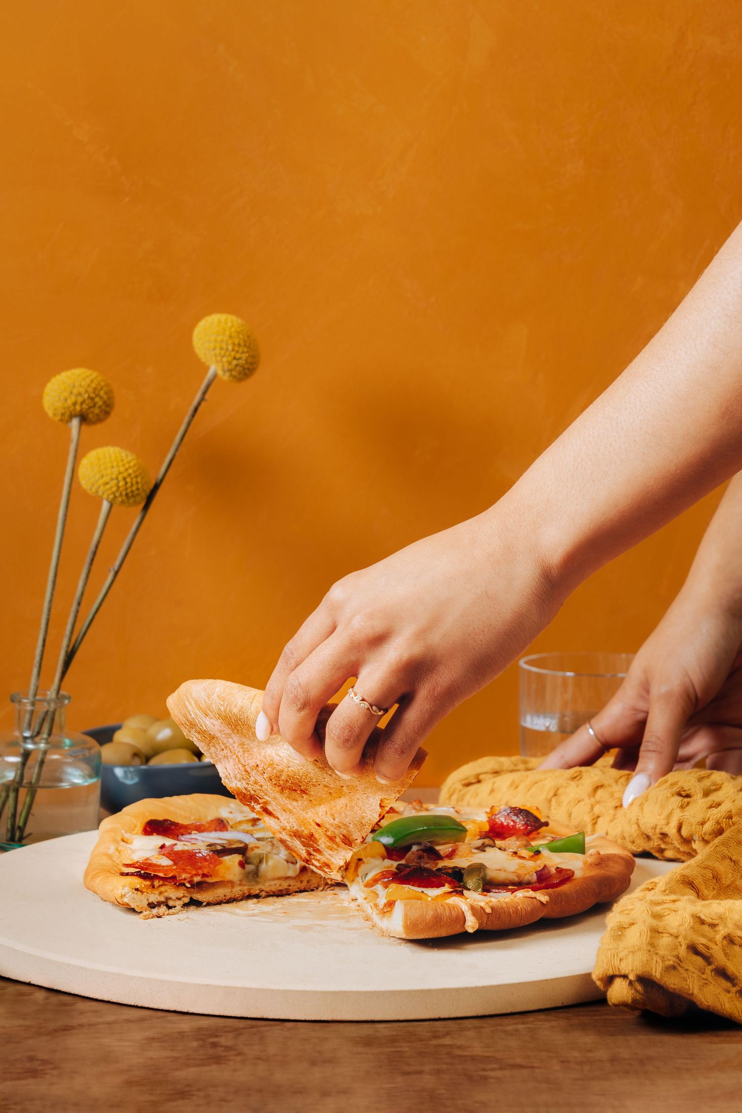 Hands arranging sandwiches on a white plate with yellow flowers in the background.