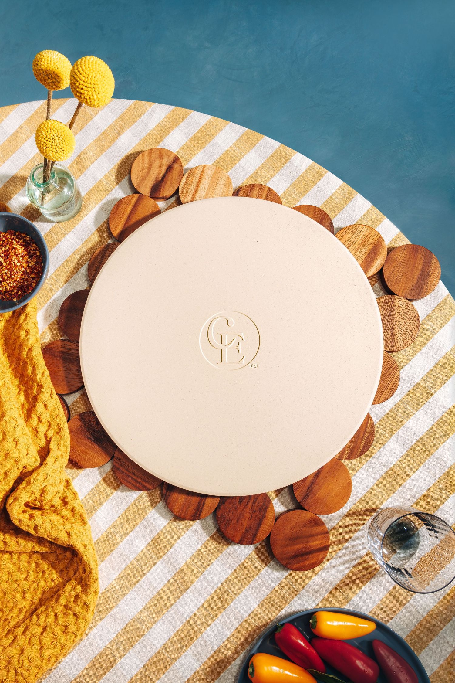 Overhead view of ceramic pizza stone on wooden trivet with yellow flowers and striped tablecloth.