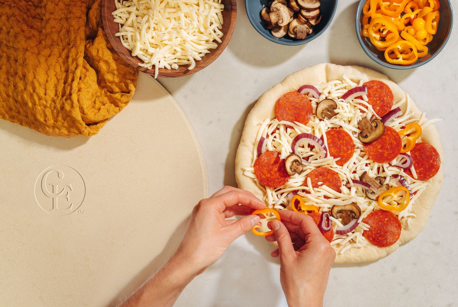 Hands preparing homemade pizza with pepperoni toppings and shredded cheese.