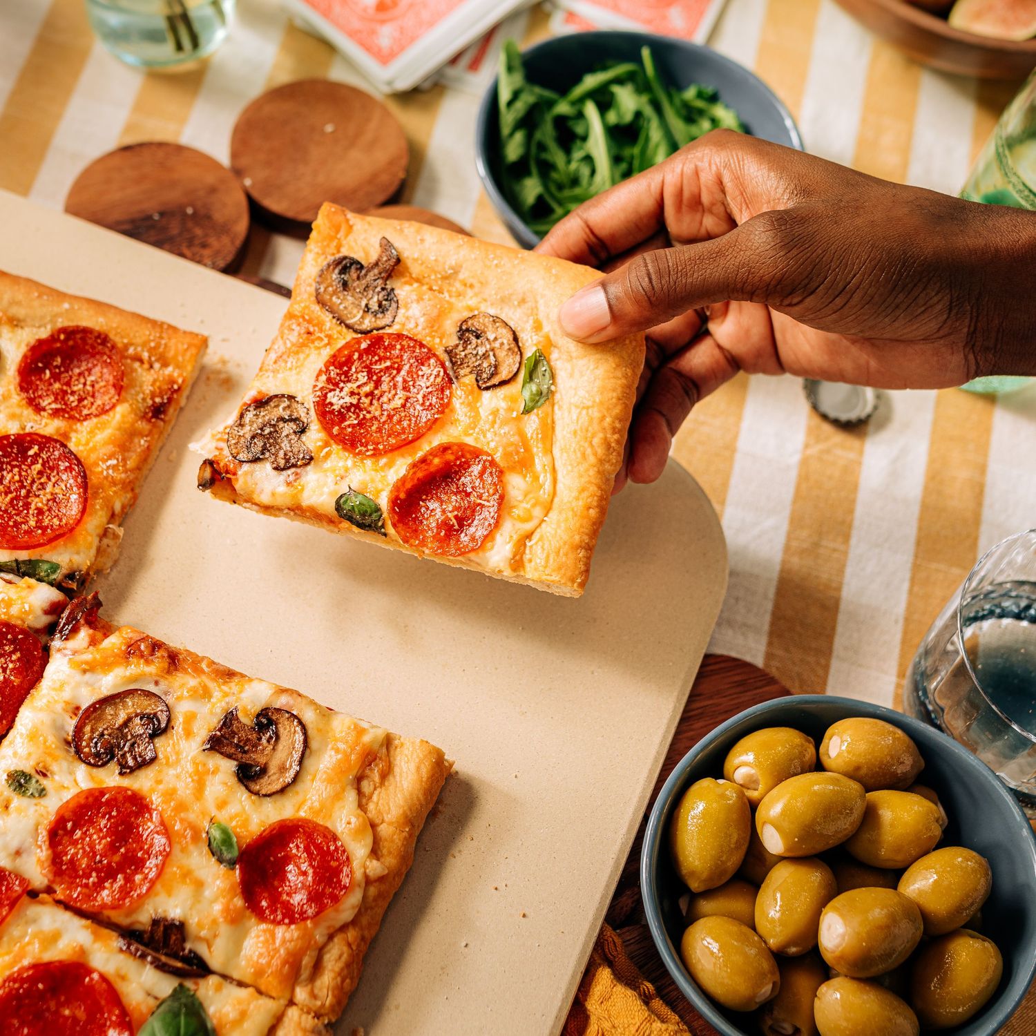 Square pizza slices with pepperoni and mushrooms served with olives and green salad.