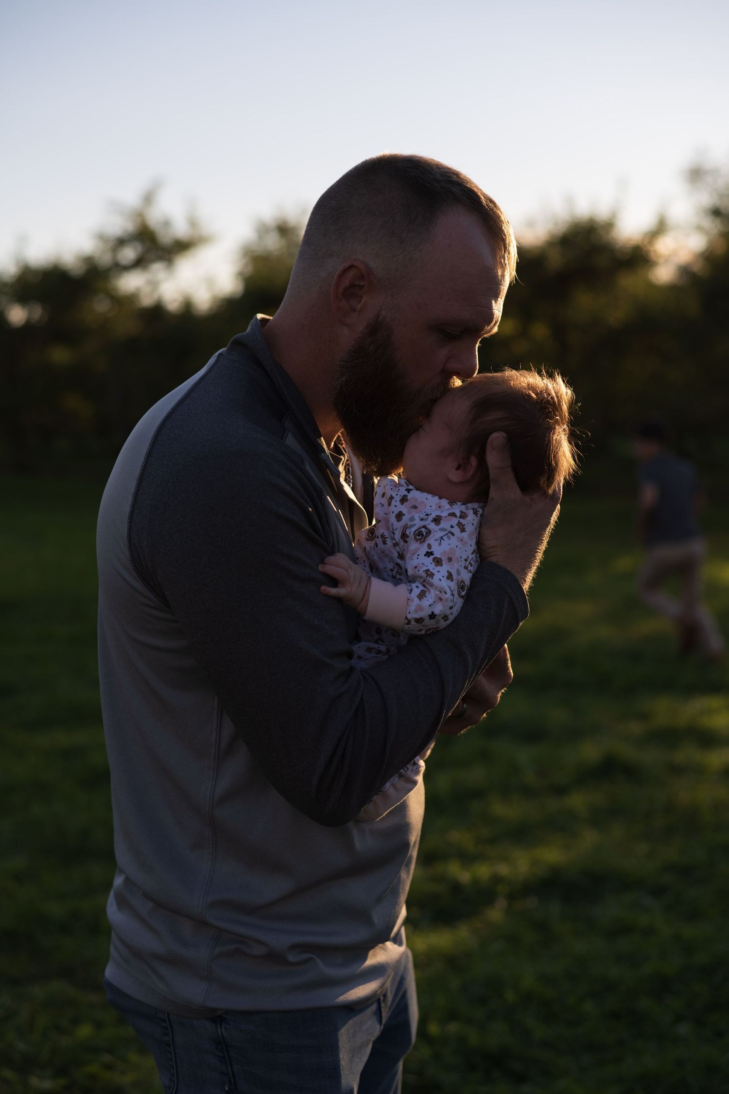 a dad kisses his baby girl on the forehead in an apple orchard during sunset