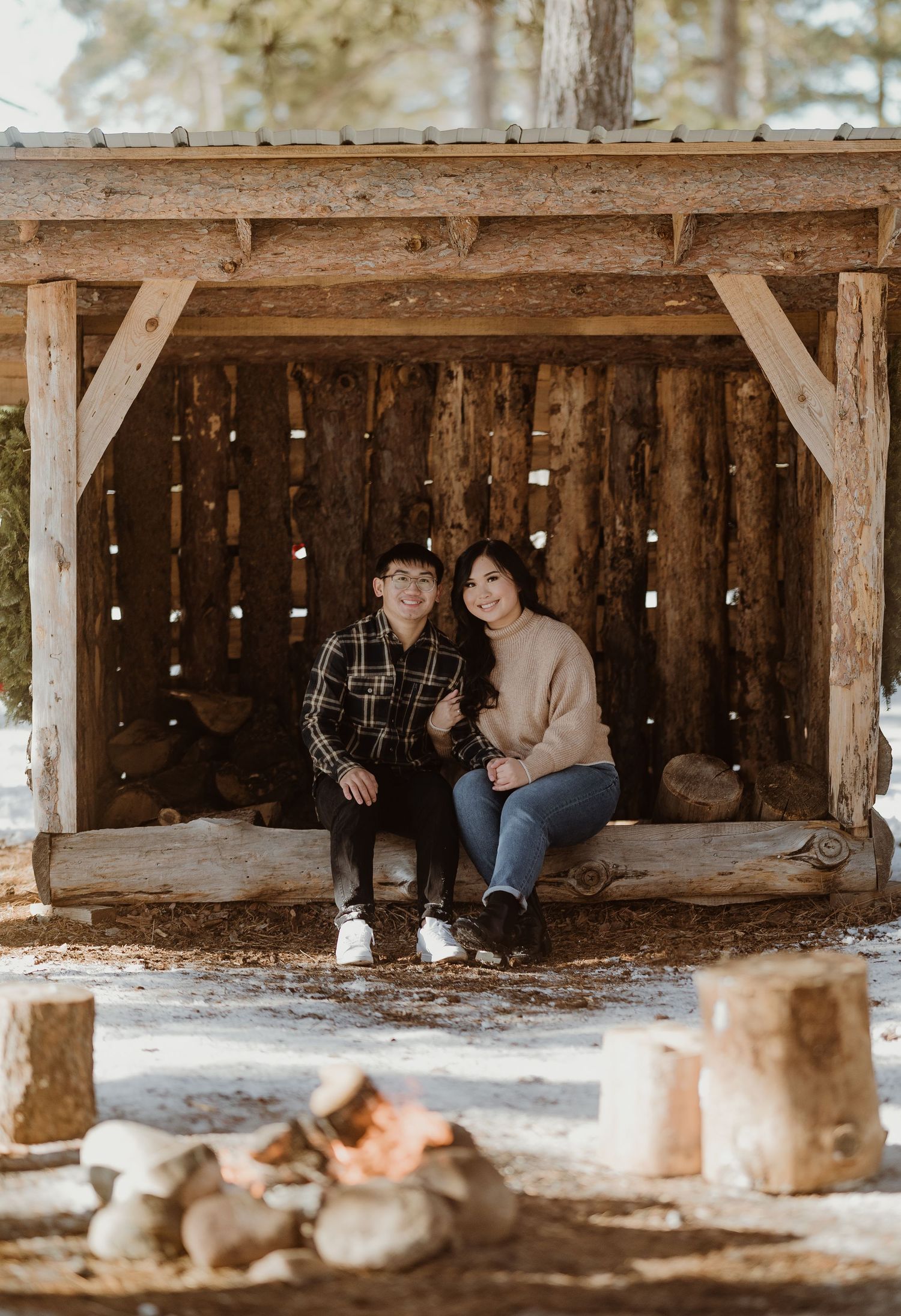 A couple sits together in a cozy wooden shelter decorated with twinkling lights in winter.