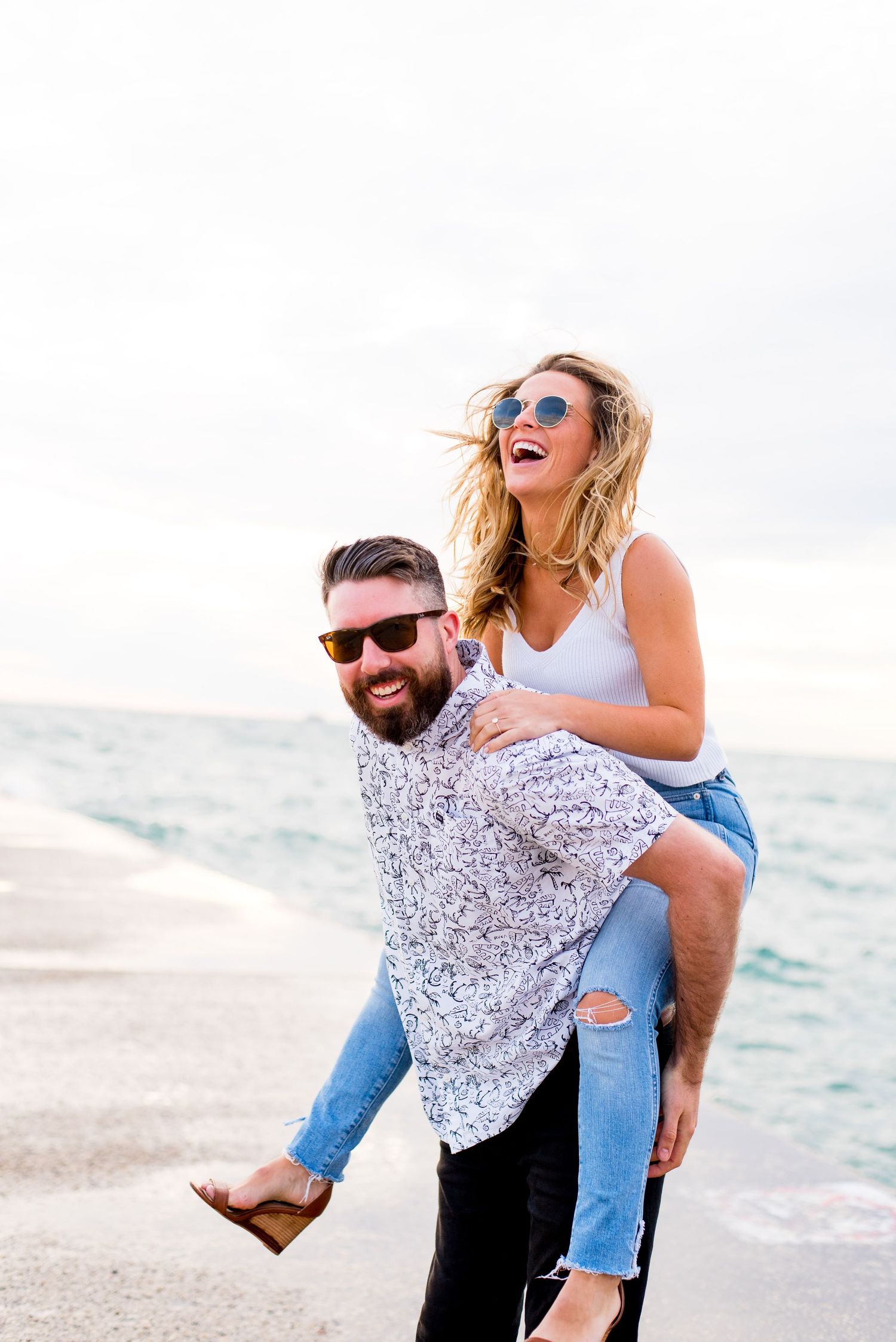 woman in white tank top and sunglasses piggyback riding on her dark haired fiance in sunglasses at North Avenue Beach