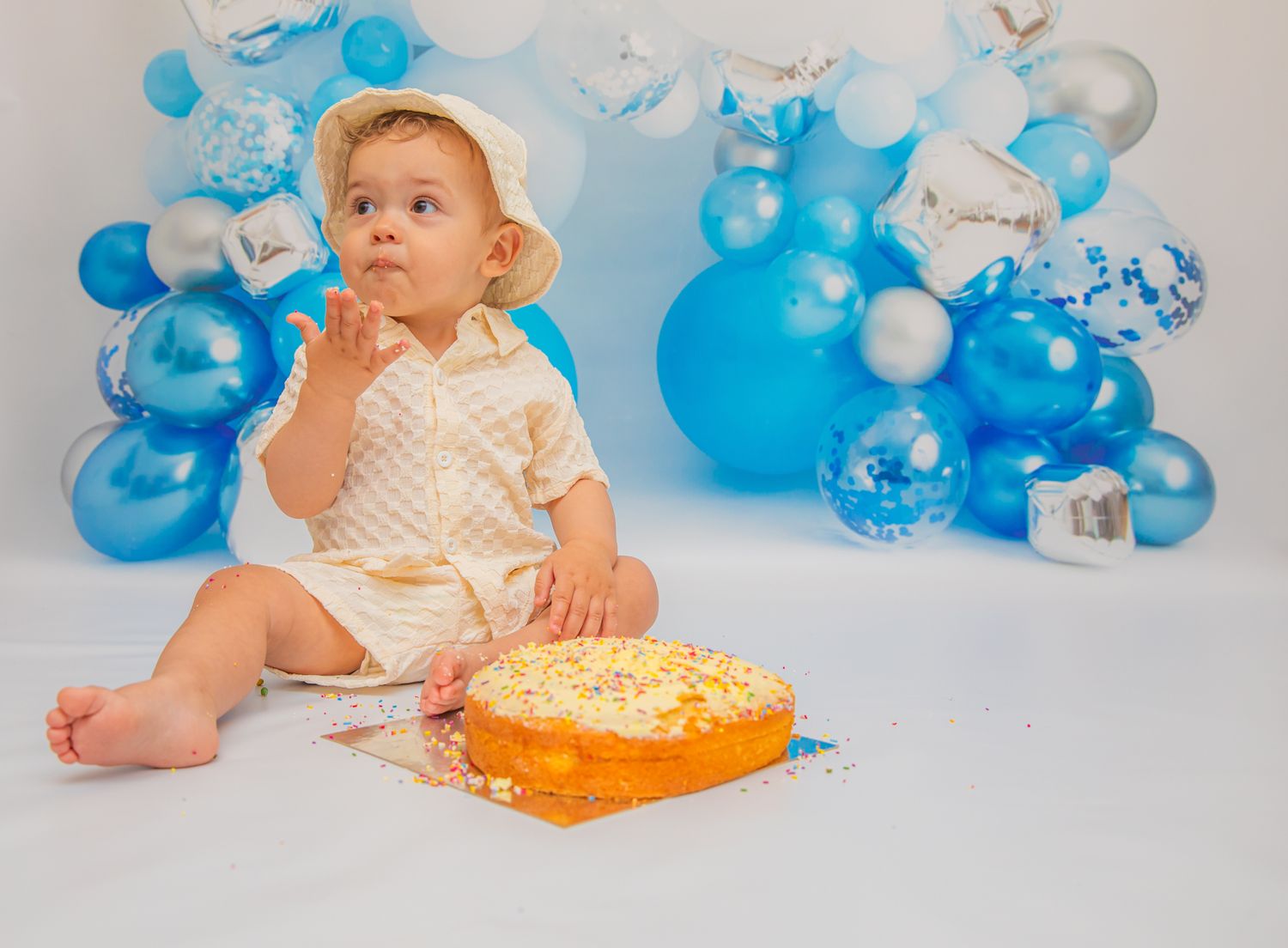 First birthday setup with orange cake and blue balloon arch backdrop for cake smash photo session.