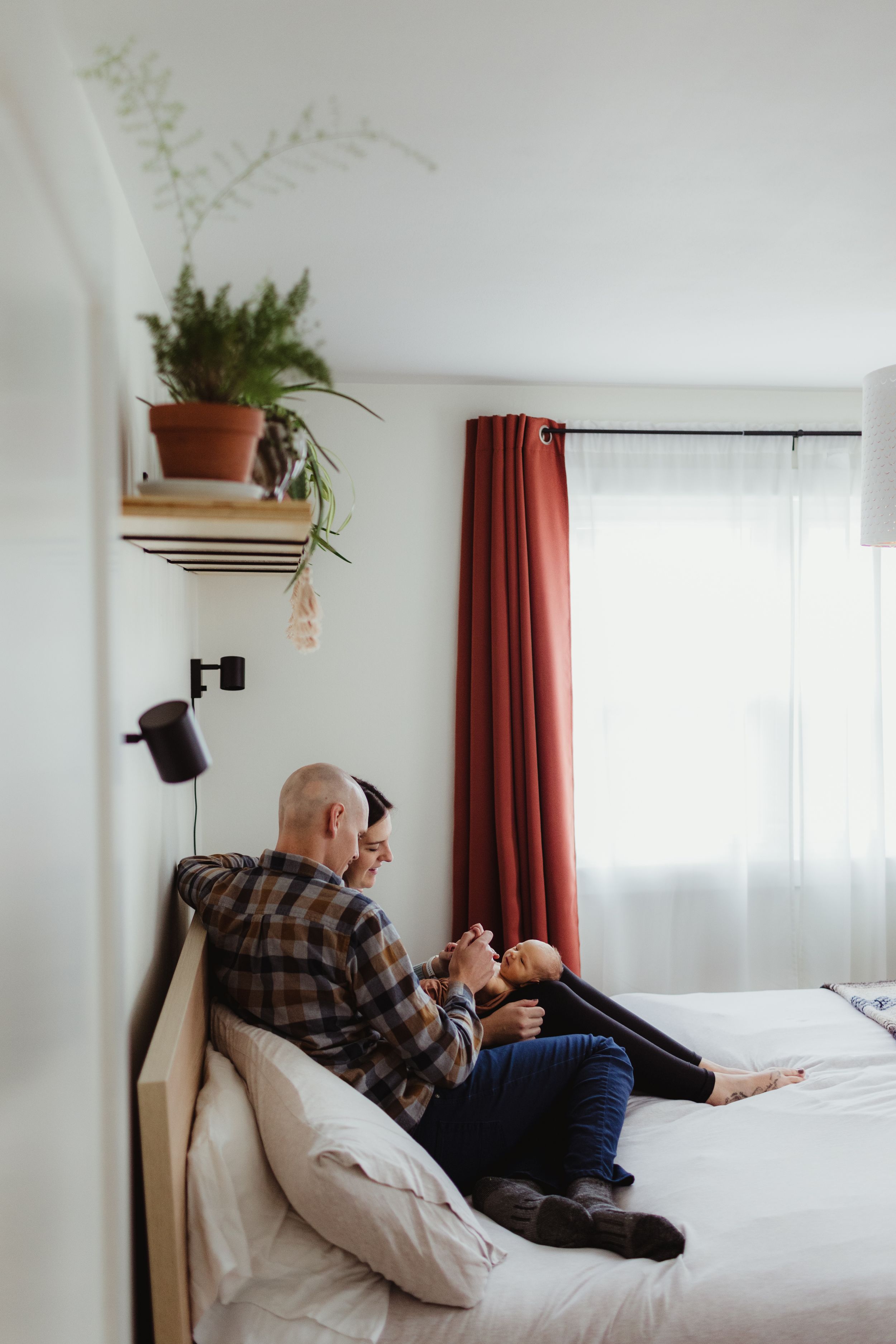 A new mom and dad snuggle on their bed with their newborn. Photo by newborn photographer, Elizabeth Pachniak Photography