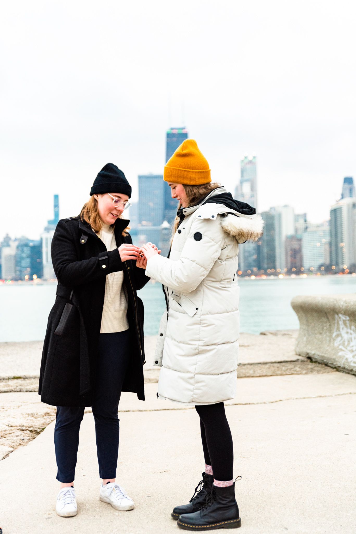 woman in black coat putting engagement ring on her girlfriend at North Avenue Beach proposal
