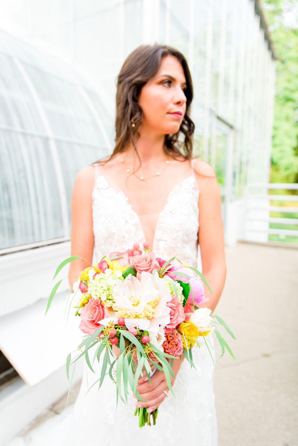 bride holding pink and yellow peony wedding bouquet in front of Krohn Conservatory at summer wedding in Cincinnati