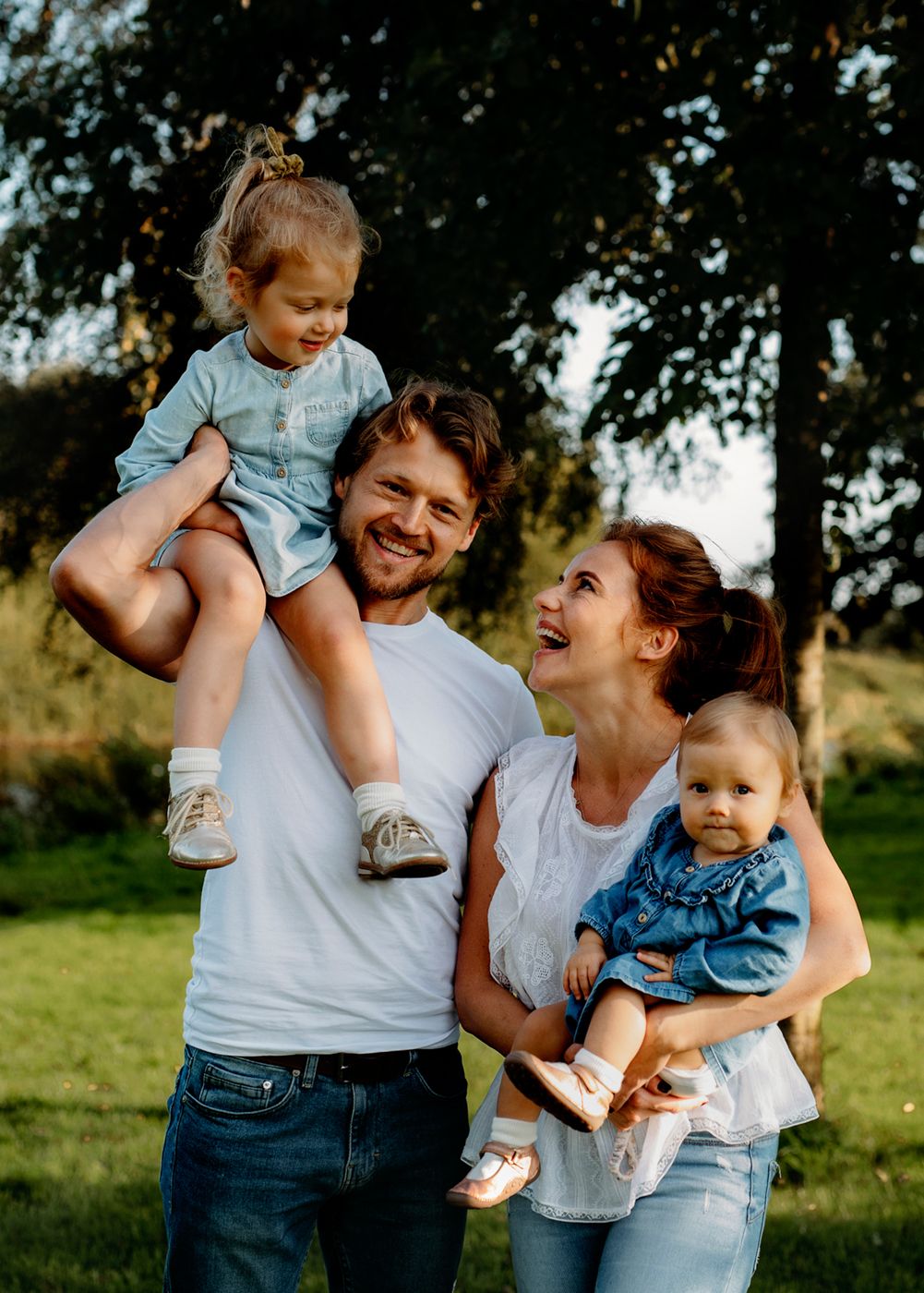 A happy family of four enjoys a walk in a sunlit park, surrounded by lush greenery. Family photoshoot in Ireland.
