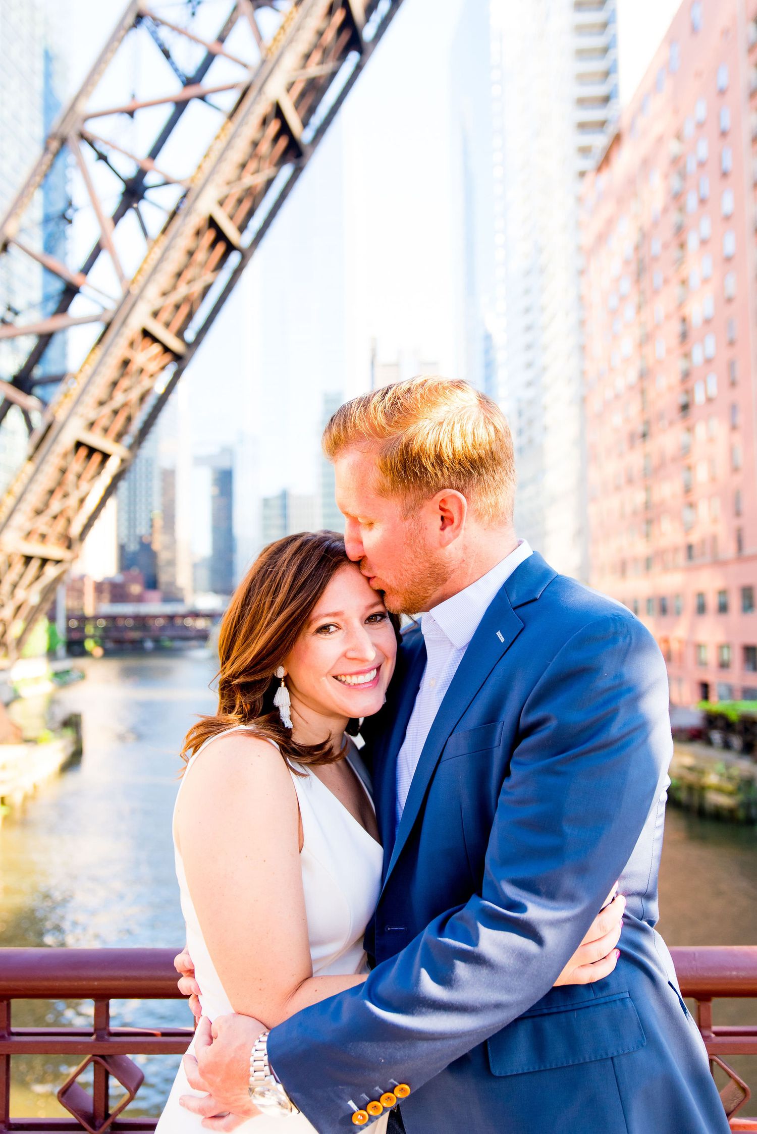 man in navy suit and woman in white dress hugging in front of Chicago River for sunset engagement pictures in Chicago