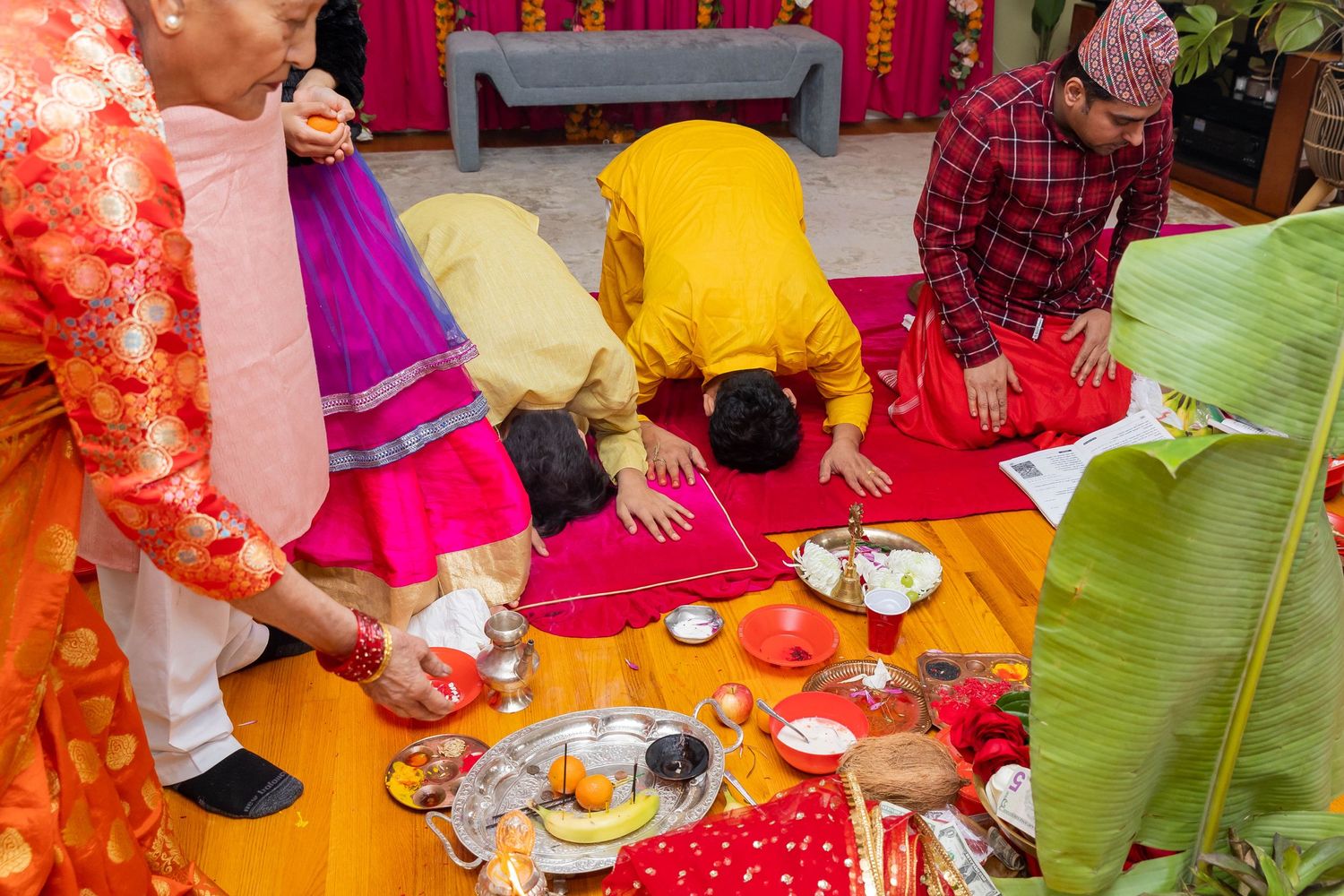 Traditional Hindu ceremony with colorful attire and ritual items laid out on floor.