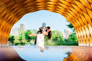 man in suit dipping and kissing woman under Honeycomb at Lincoln Park for engagement pictures in Chicago at sunset