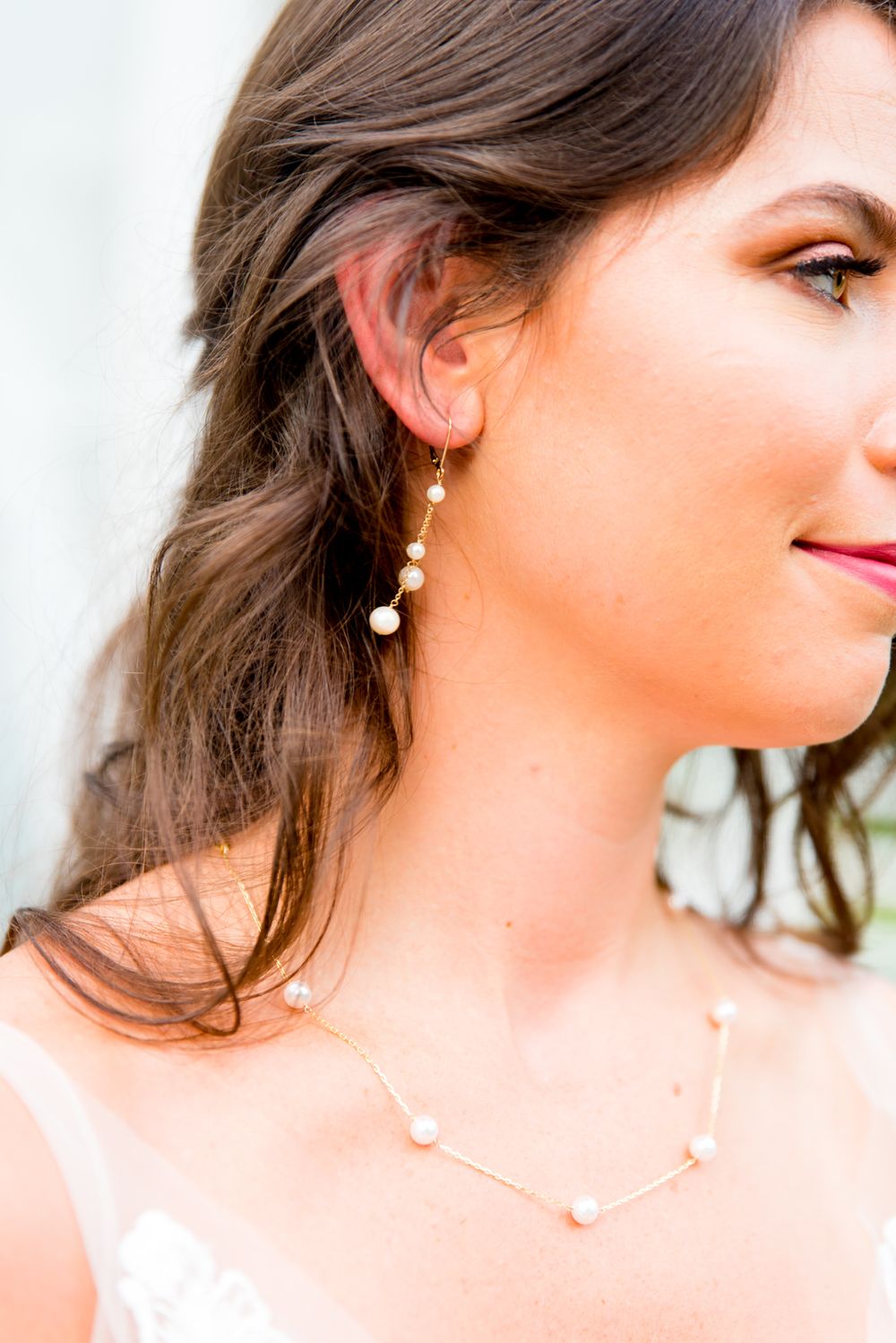 profile of brown haired bride wearing gold peal dangle earrings and gold pearl necklace for wedding