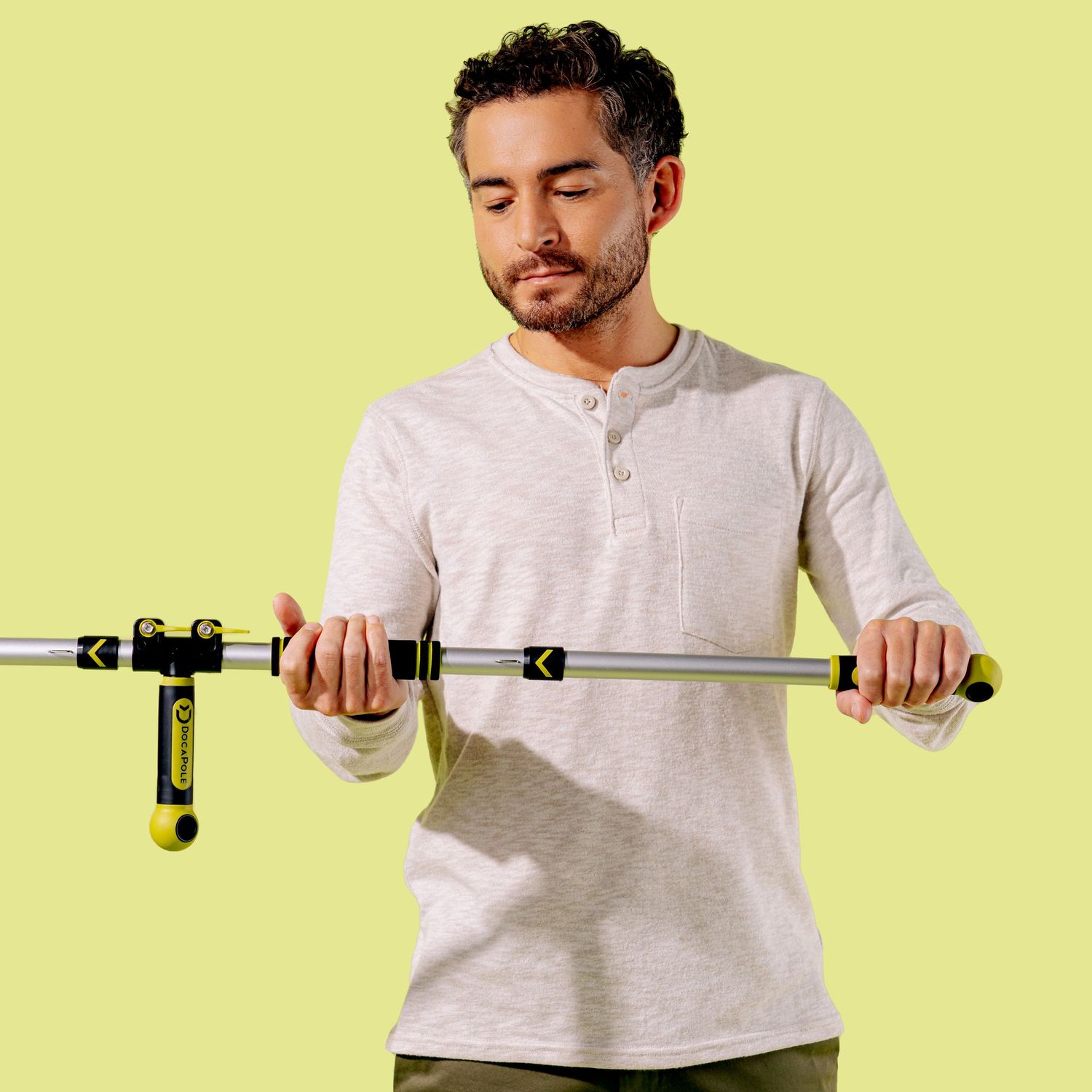 Person demonstrating proper grip technique on an extendable cleaning pole against yellow background.