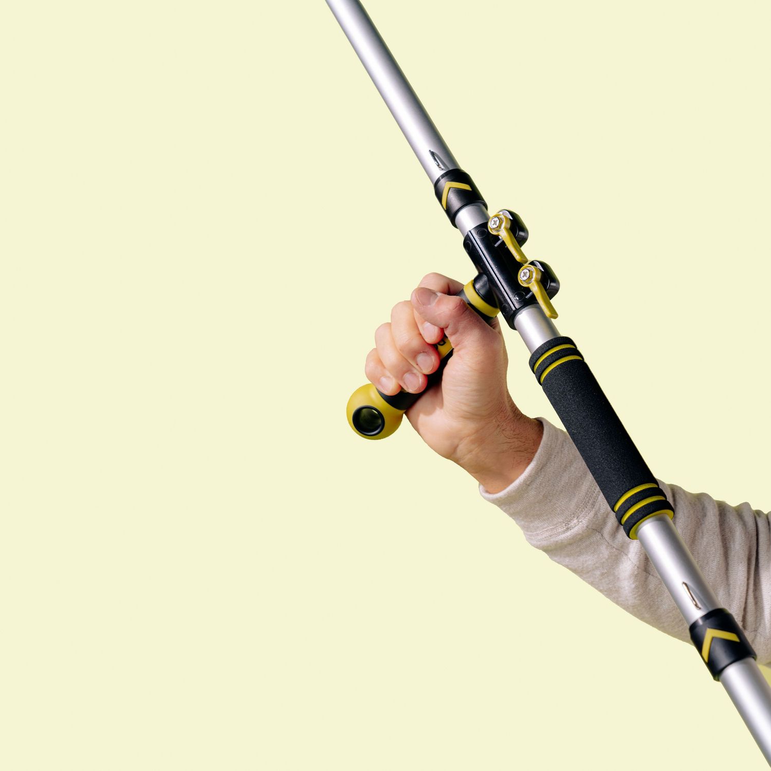 Hand gripping extendable cleaning pole against bright yellow background.