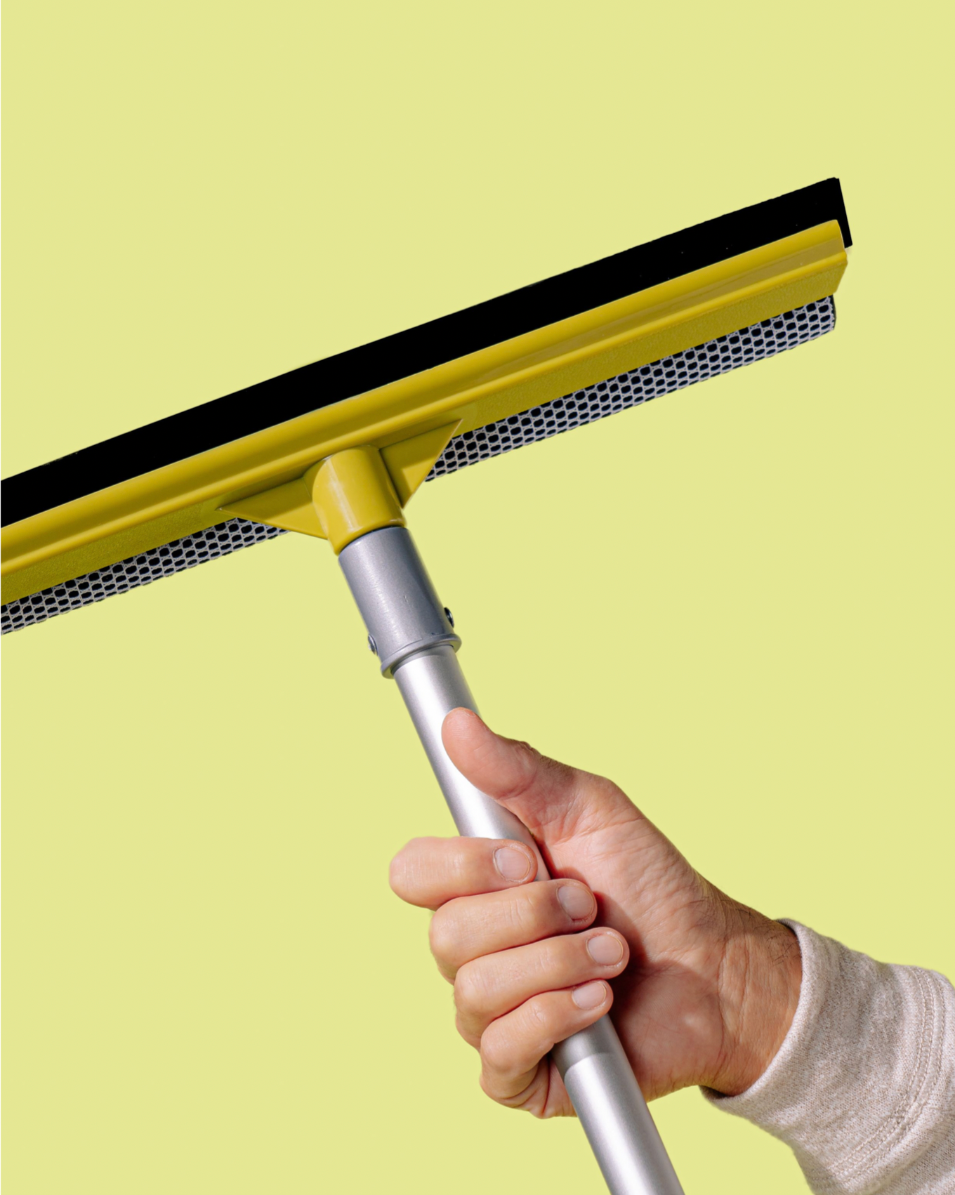 Hand holding a yellow window squeegee cleaning tool against pale yellow background.