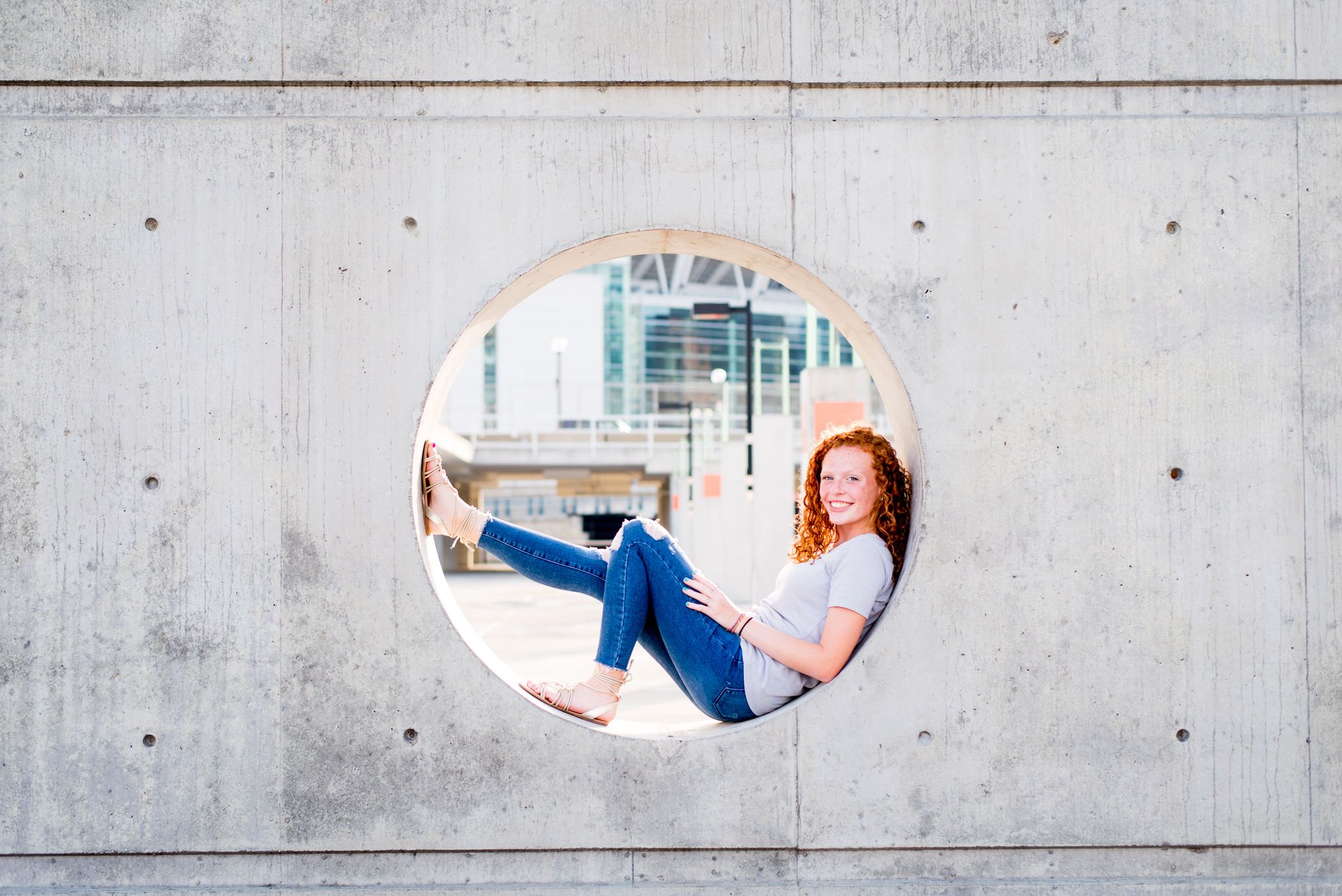 young woman with red curly hair sitting inside a circle cut out of concrete in a Cincinnati parking garage