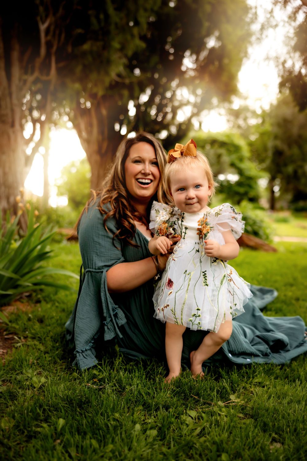 Two people share a joyful moment sitting on grass in a sunlit garden with beautiful bokeh lighting effects.